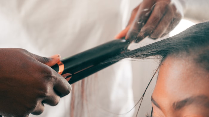 Hands guiding a flat iron through long dark hair during a smoothening treatment