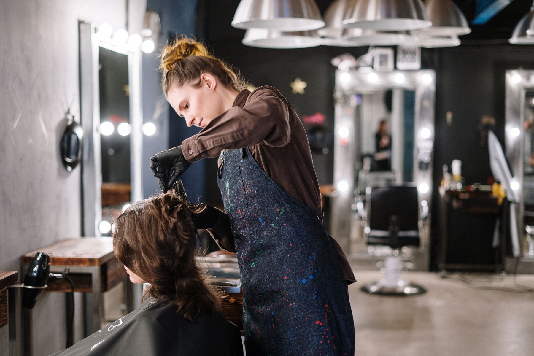A stylist sectioning and working through a client's hair under warm bulb lighting in a salon