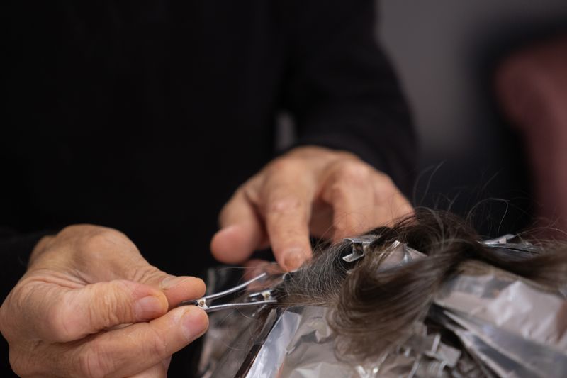 A stylist sectioning dark hair into foils during a highlighting service.