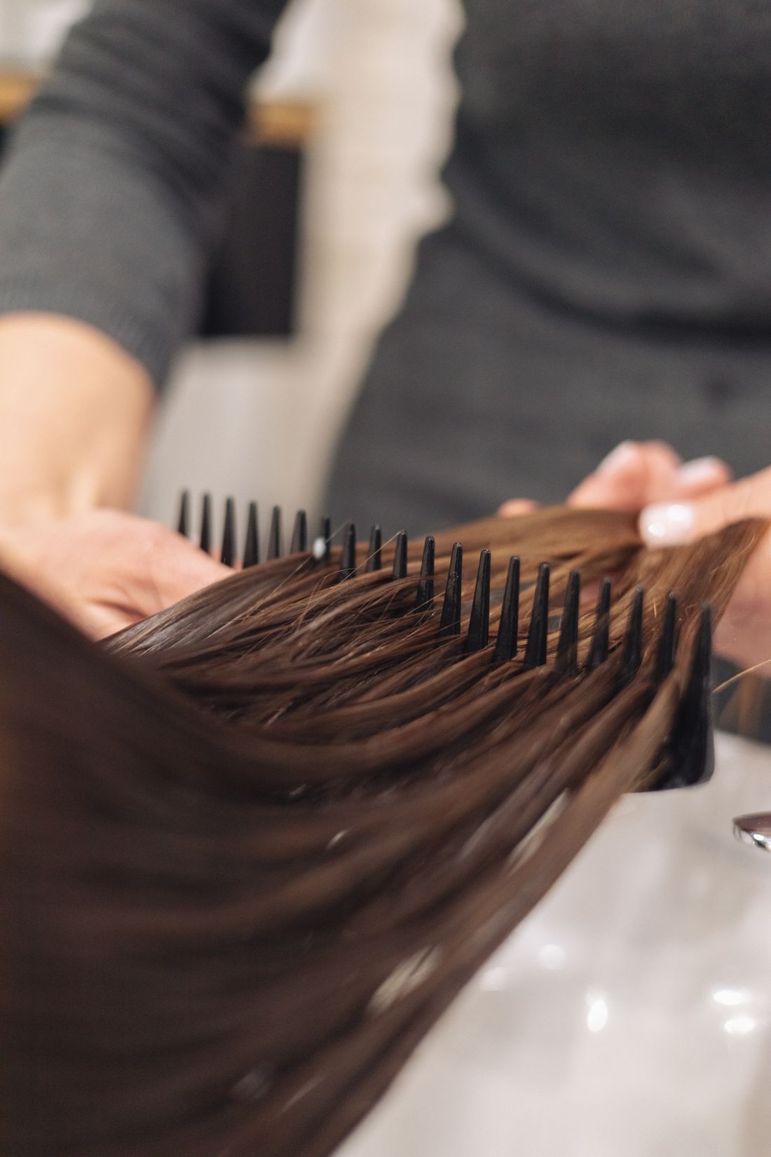 A wide-tooth comb drawn cleanly through long, glossy, freshly smoothed hair.