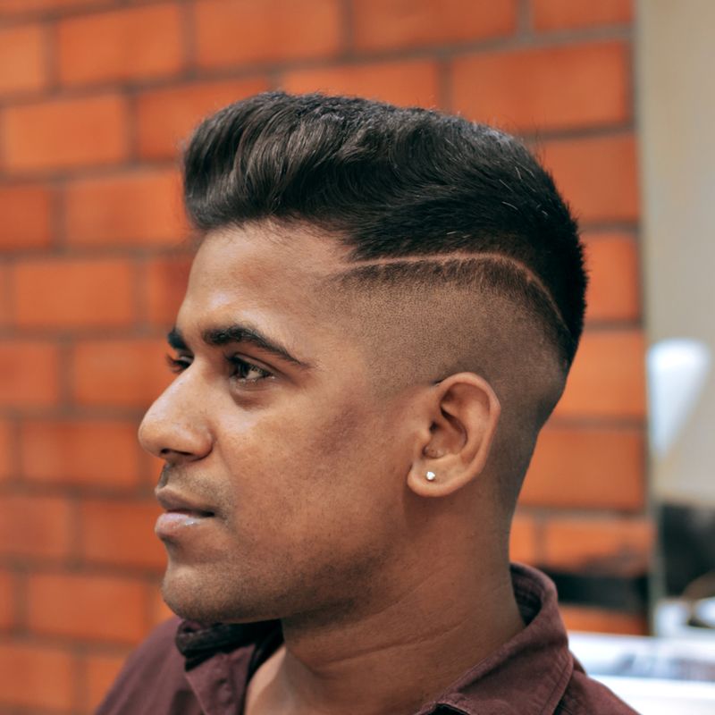 A sharp high fade on a young man, photographed in profile against a brick wall.