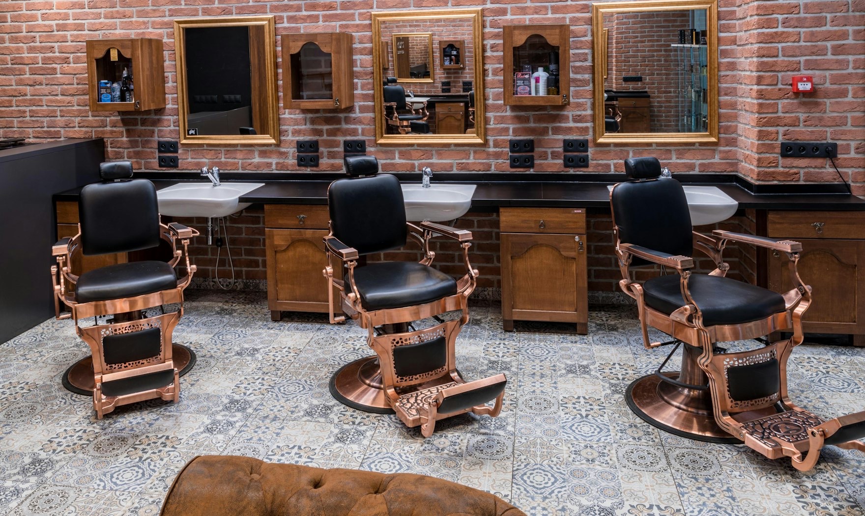 A warm salon floor — exposed brick, copper styling chairs and brass-framed mirrors