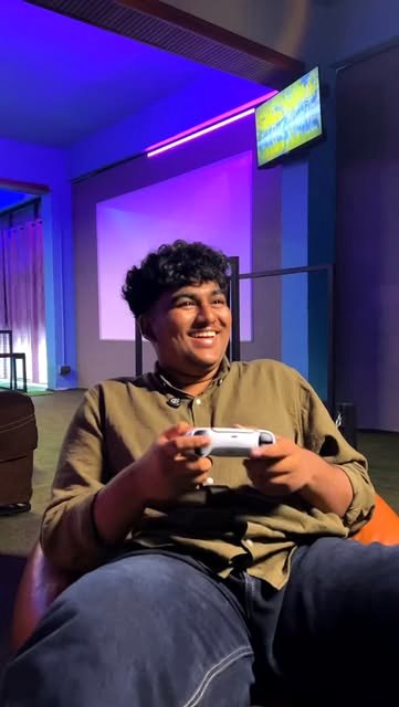 A young gamer smiling with a PS5 controller in the neon-lit lounge