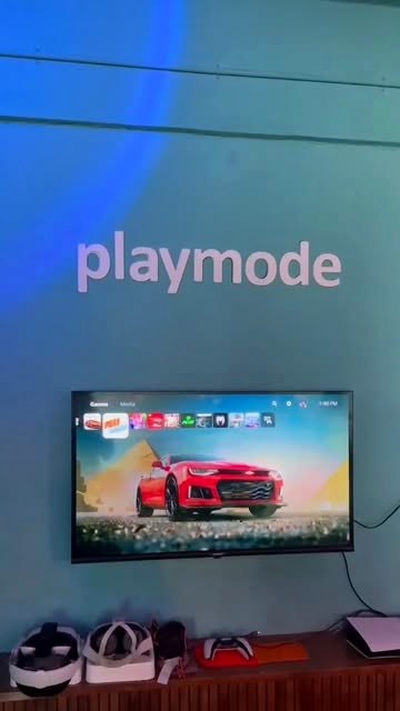 The glowing playmode wall sign above a PS5 racing game on the big screen