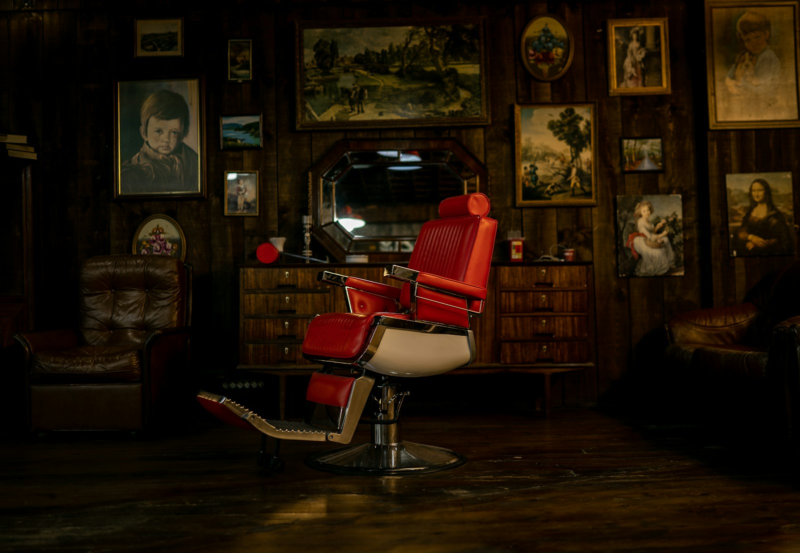 A vintage red-leather barber chair in a wood-panelled hall, framed pictures on the wall