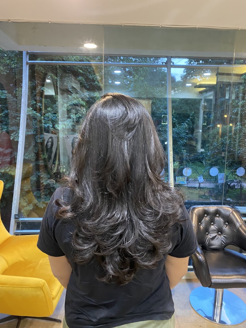 Long hair blow-dried into soft bouncy layers, shot by the salon's glass front