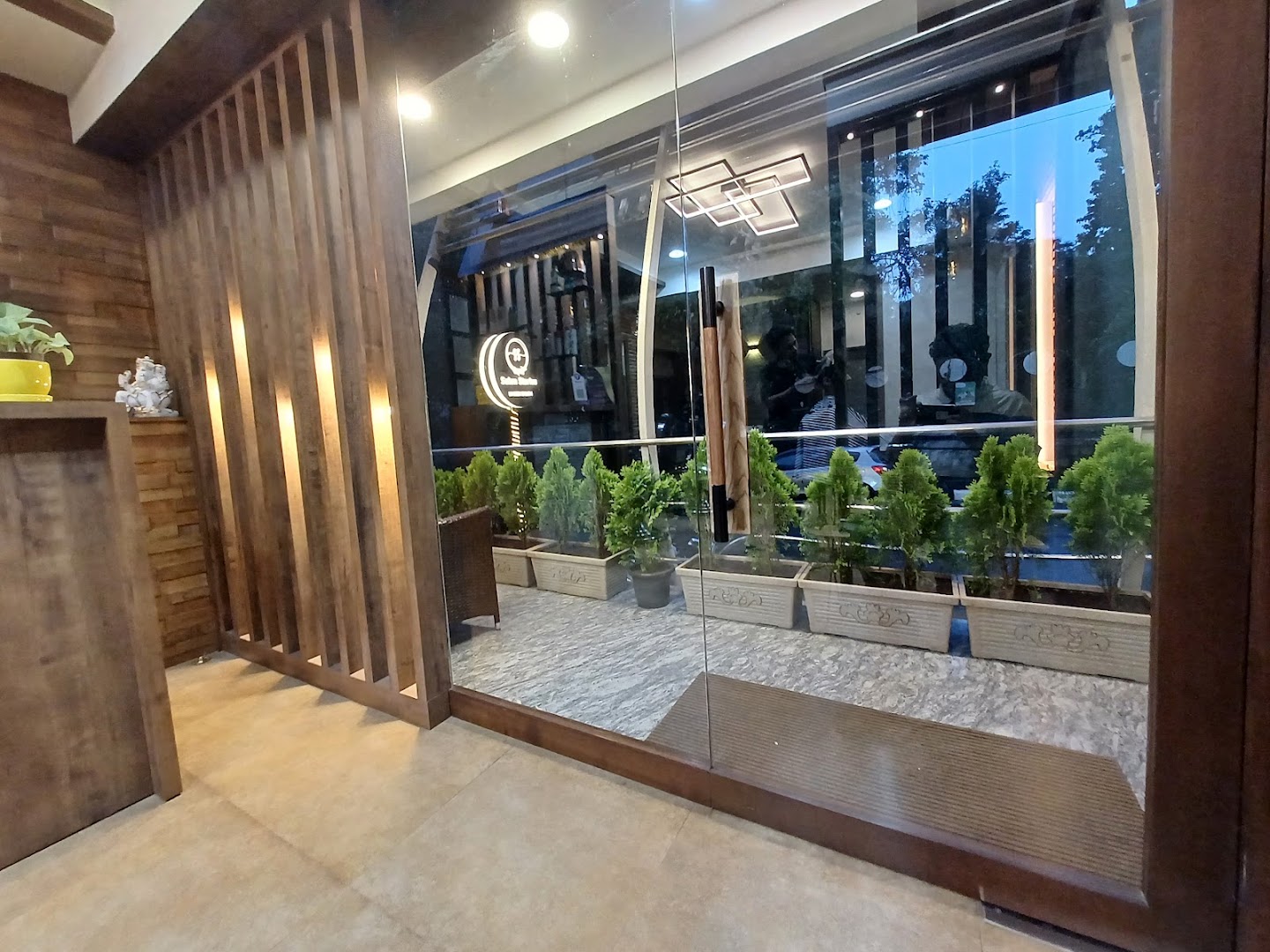 The glass-front entrance walkway, lined with planters and warm slatted wood