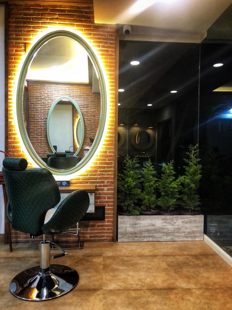 A backlit oval halo mirror glowing against the brick wall, over a deep-green quilted styling chair