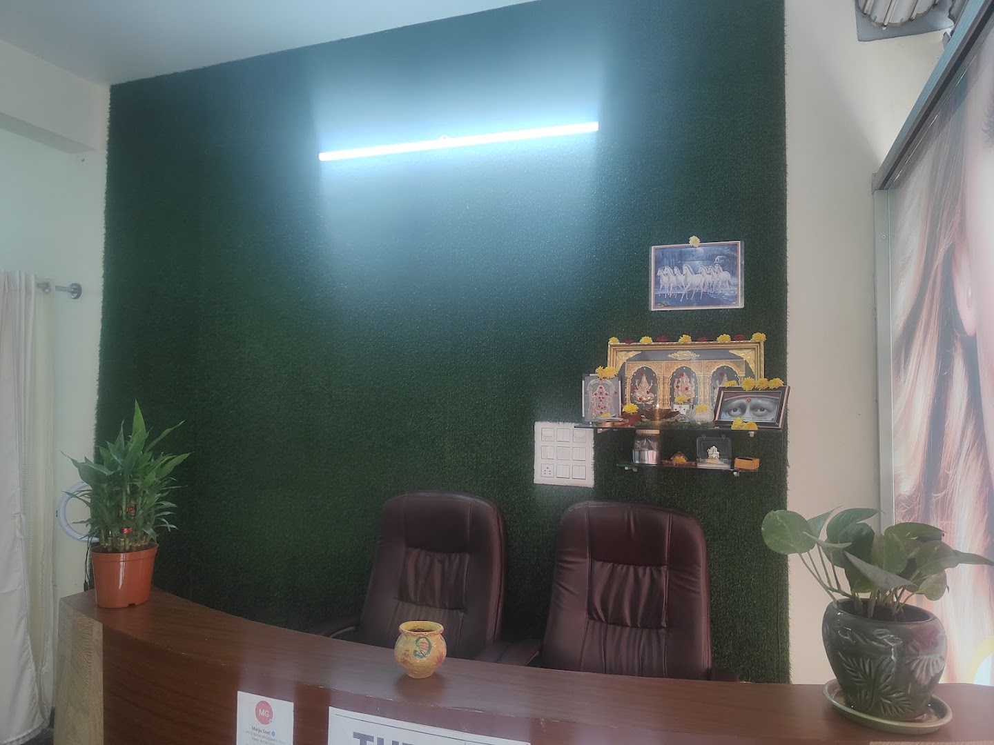 The reception at Siri Spa and Salon — a deep-green grass wall behind the wooden desk, with plants and a small shrine