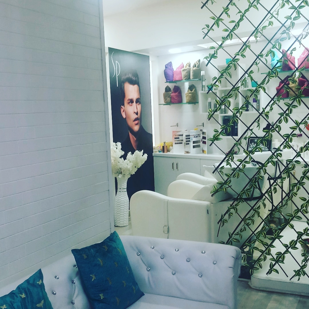 The men's grooming corner at STUDIO@11: a barber chair beneath a portrait mural, greenery trellis to the side.